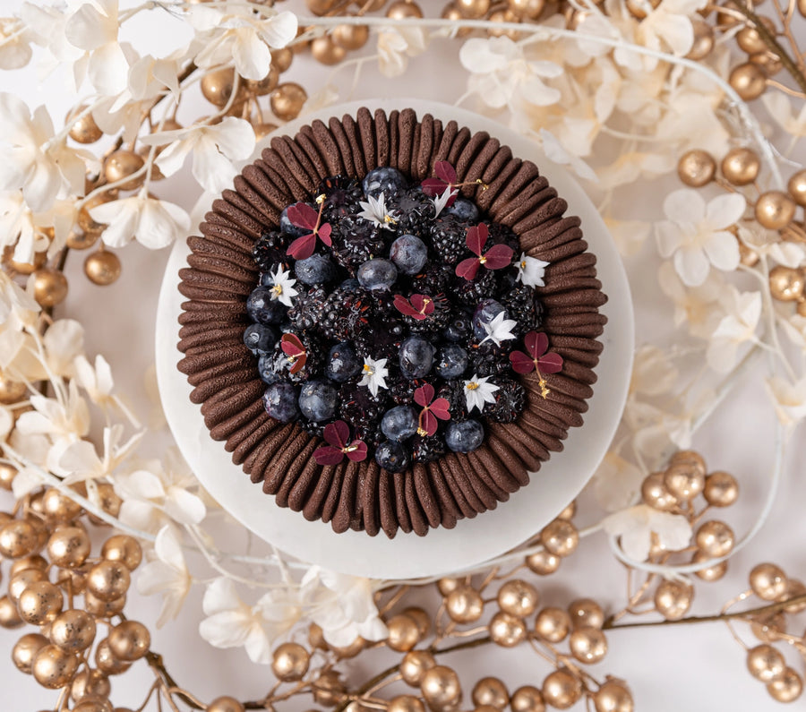 Chocolate dessert with berries and flowers on a decorative background with gold and white elements.