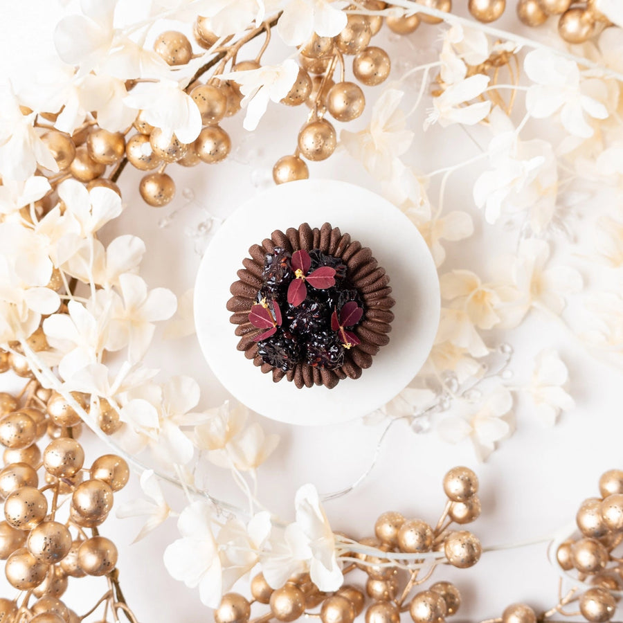 Chocolate truffle with berries on a white plate surrounded by gold and white decorative elements