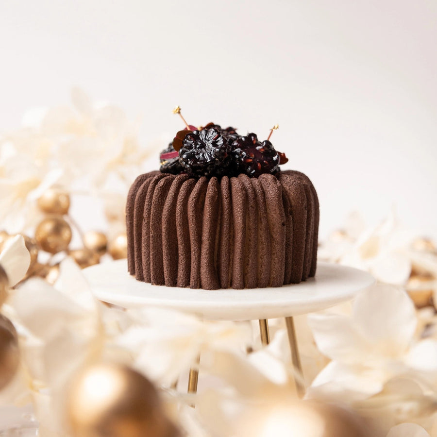 Chocolate cake with cherries on a white stand against a light background