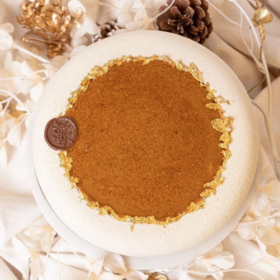 Round brown treat with a white rim on a decorative background with flowers and pinecones.