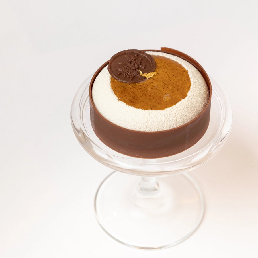 Dessert with chocolate, caramel, and white layers on a stand against a white background
